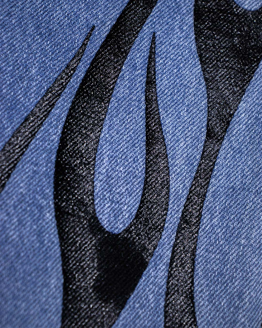 Cận cảnh vải denim xanh, họa tiết đen trừu tượng như ngọn lửa.