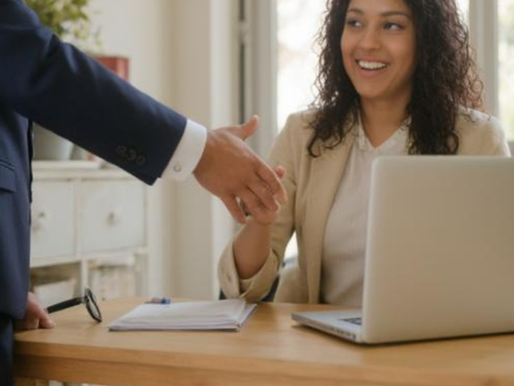 Une candidate souriante serre la main d'un recruteur lors d'un entretien professionnel, assise à un bureau avec un ordinateur portable, symbolisant une connexion humaine au cœur du processus d'embauche.