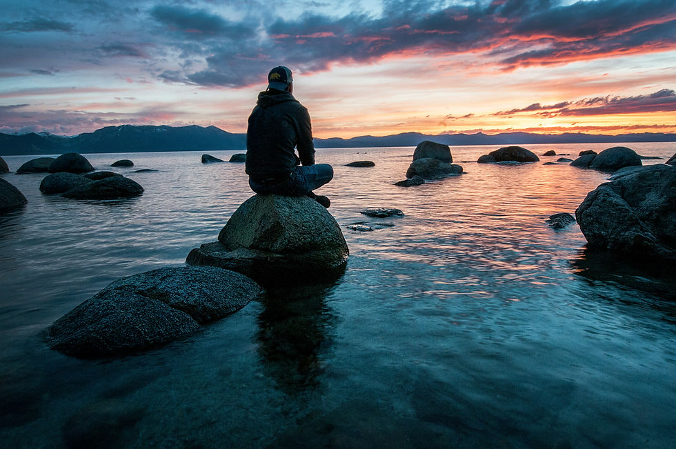 Man sitting on rock by water watching sunset