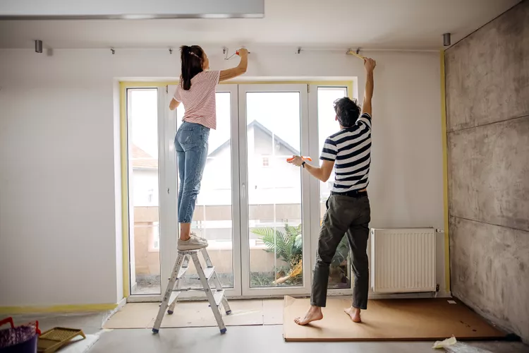 two people painting a wall inside a house