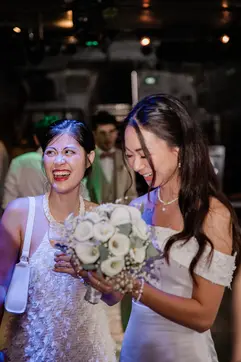 Two women, one holding a bouquet of white flowers, at a nighttime event.