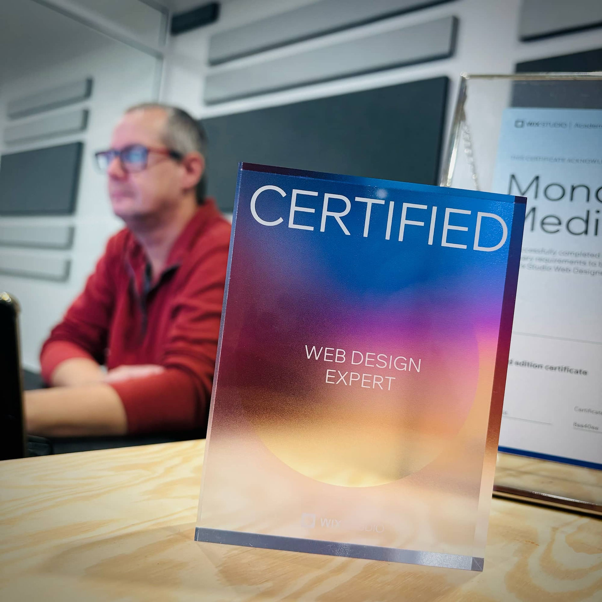 Wix Studio Certified Web Design Expert award plaque on a desk at Monday Media, with team member working in the background in the Perth studio.