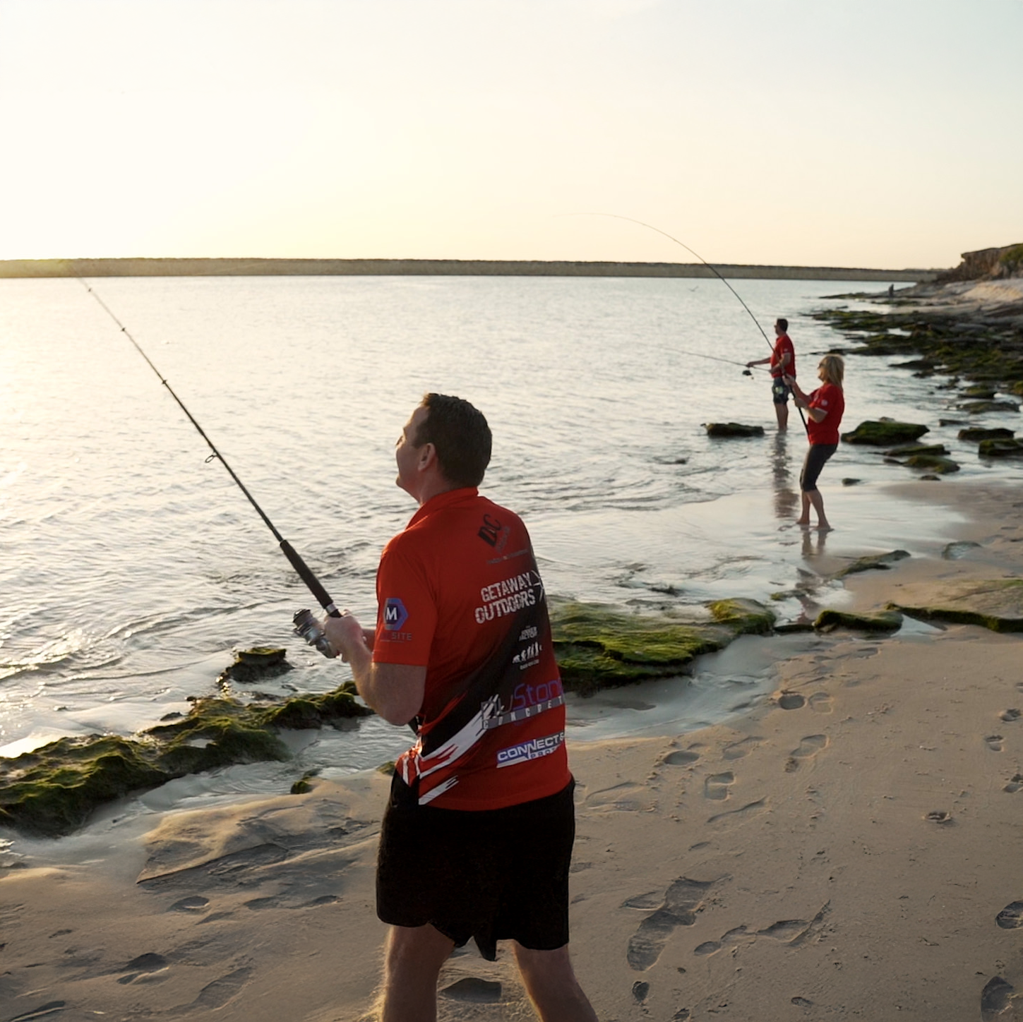 Person casting a fishing line on a sandy beach at sunset