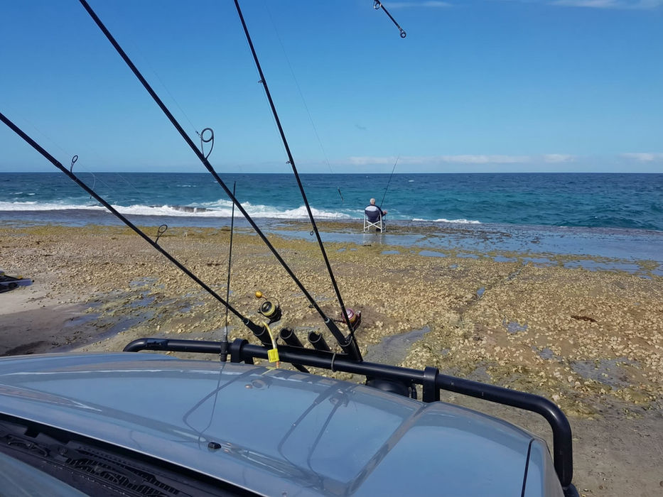 Person fishing by the ocean with rods on a car roof rack