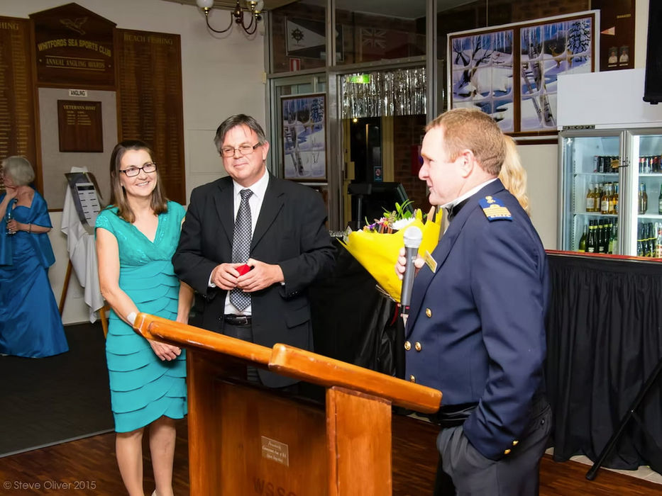 Man in uniform speaks at a podium with two people listening