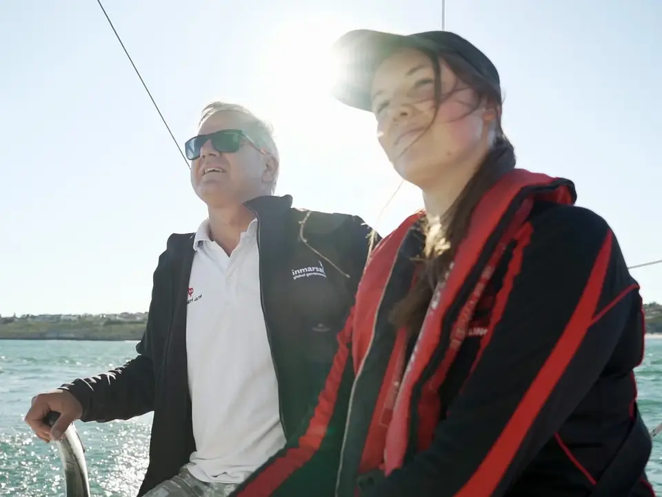 Man steering sailboat with woman in life jacket