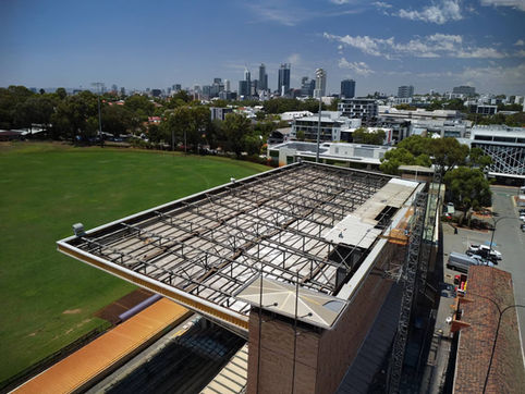 Aerial view of a building under structural inspection in Perth with exposed roof framing and city skyline.