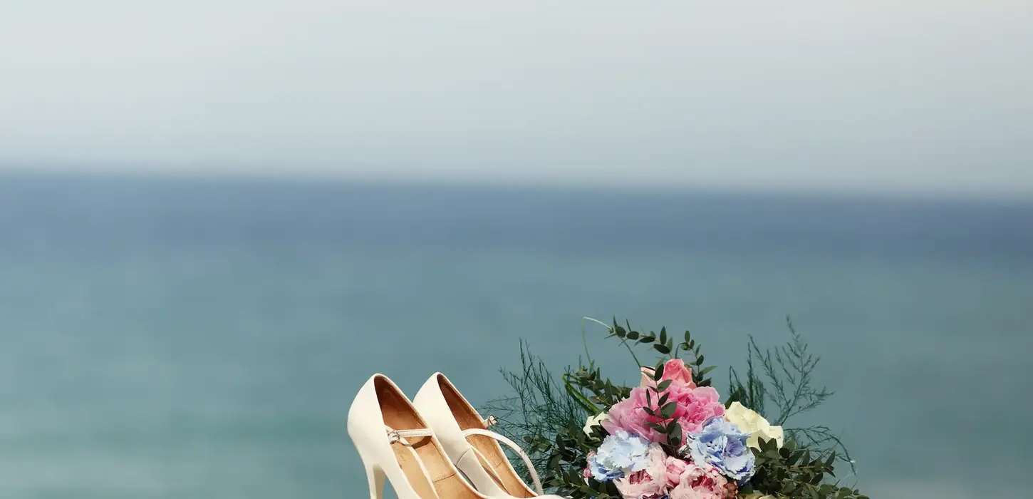 White wedding shoes and floral bouquet by the ocean