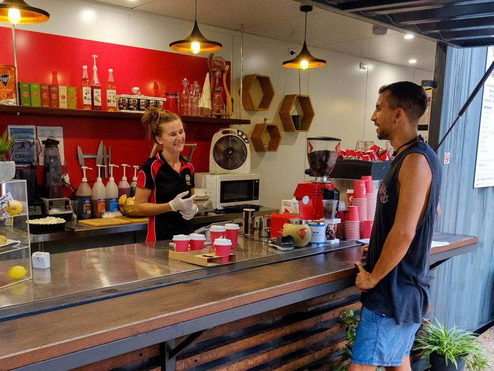 Barista serving a customer at a cafe, counter with drinks and decor