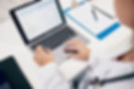 Hands typing on a laptop showing a survey. Nearby, a clipboard with a form and pen. The setting is a clean, professional office.
