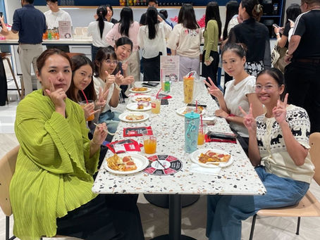People seated around a long table at JustCo in Gaysorn Amarin during a lunchtime Social Break, eating and chatting in a coworking lounge.