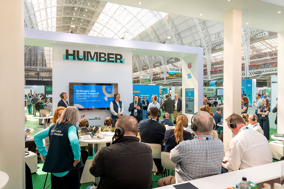 Exhibition stand labelled HUMBER at a trade show, with a seated audience listening to speakers and a large screen presentation.