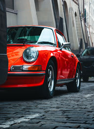 Red classic Porsche 911 parked on a cobbled street in Bern, Switzerland, shot from a low angle.