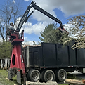 Grapple truck actively lifting and removing large tree debris at a worksite.