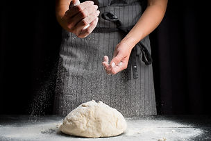 mid-shot-baker-pouring-flour-over-dough.jpg
