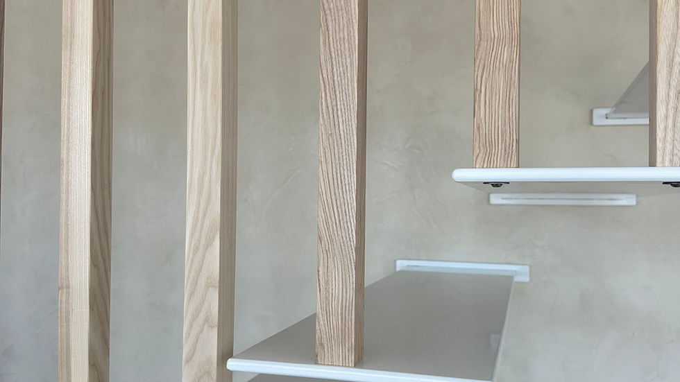 Gros plan sur l'escalier suspendu : marches métallique laquée et claustra bois sur mesure.