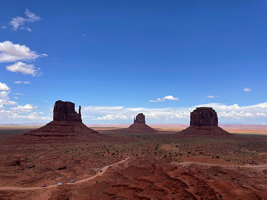 "Monument Valley landscape featuring the iconic three rock formations, with a blue sky and orange-hued rocks."