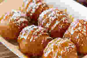 a serving tray with 6 puffy fried dough balls glazed and topped with powdered sugar