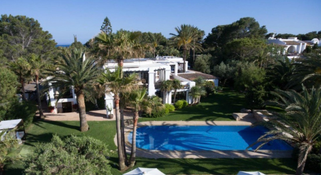 Aerial drone view of a luxury Mediterranean estate featuring a large swimming pool and lush palm tree gardens.