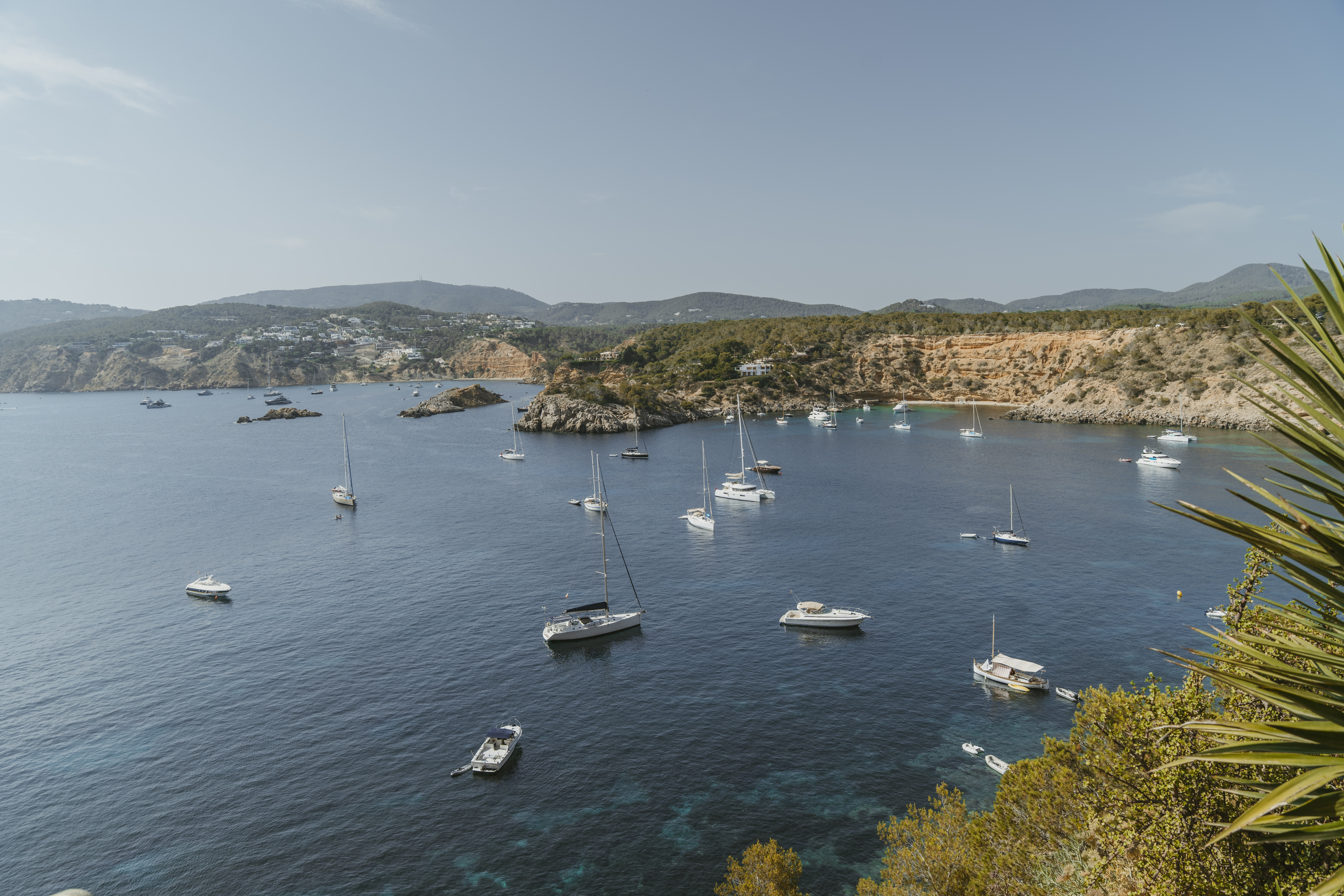 Scenic view of a Mediterranean bay with luxury yachts and sailboats anchored near an Ibiza holiday villa.