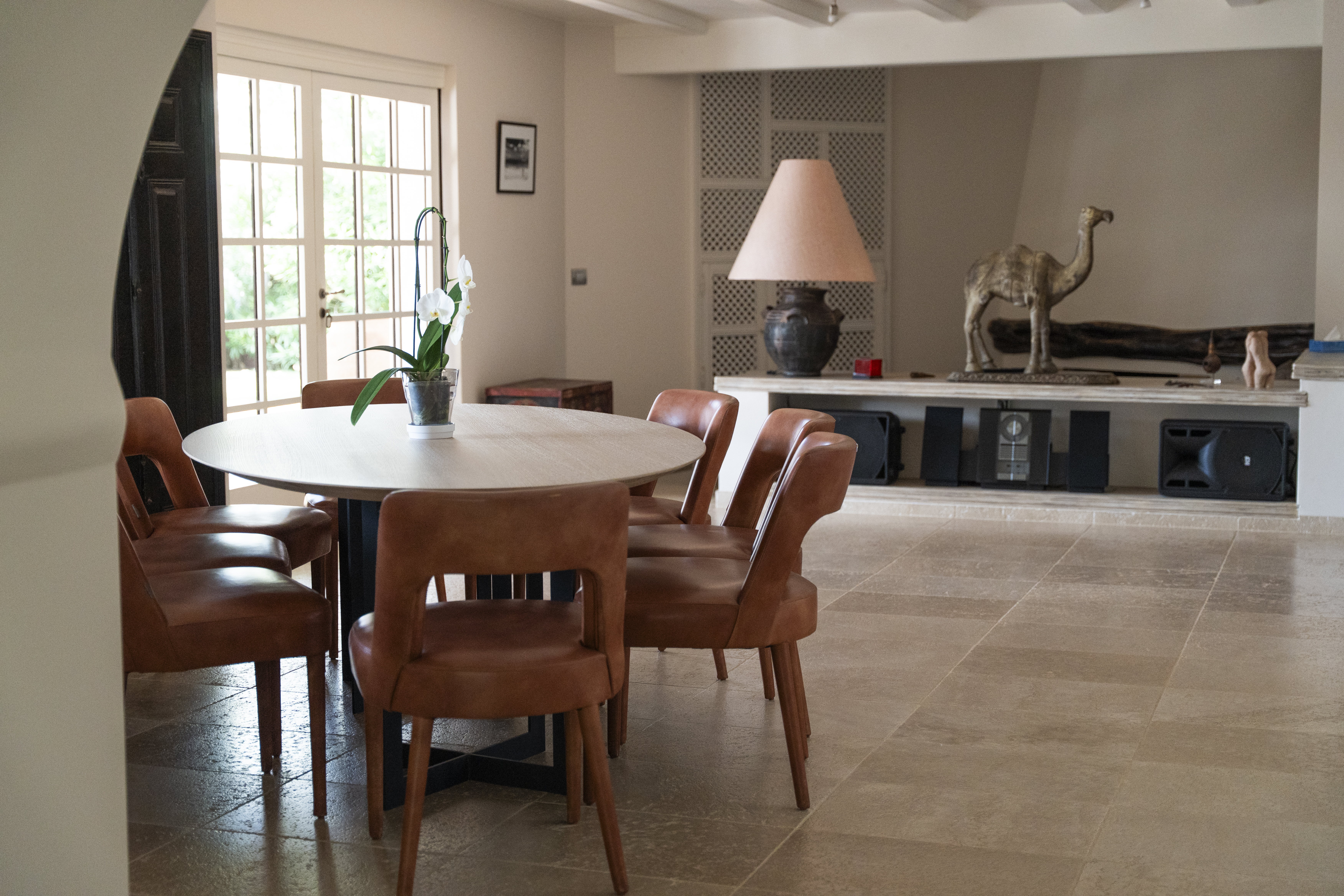 Elegant villa dining room featuring a round wooden table, tan leather chairs, and bright natural light from French doors.