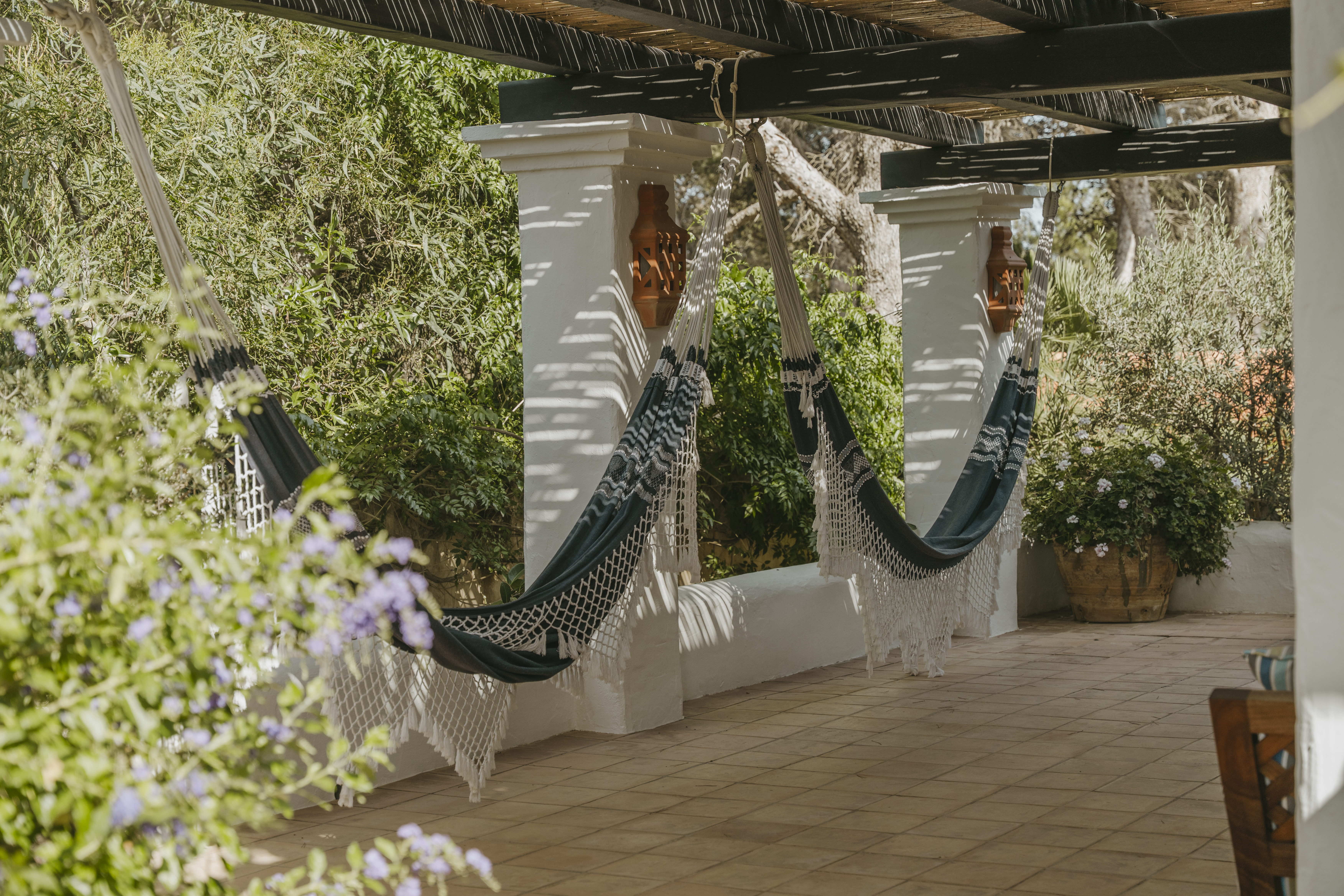 Bohemian style hanging hammocks on a shaded villa porch with terracotta tiles and lush green gardens.