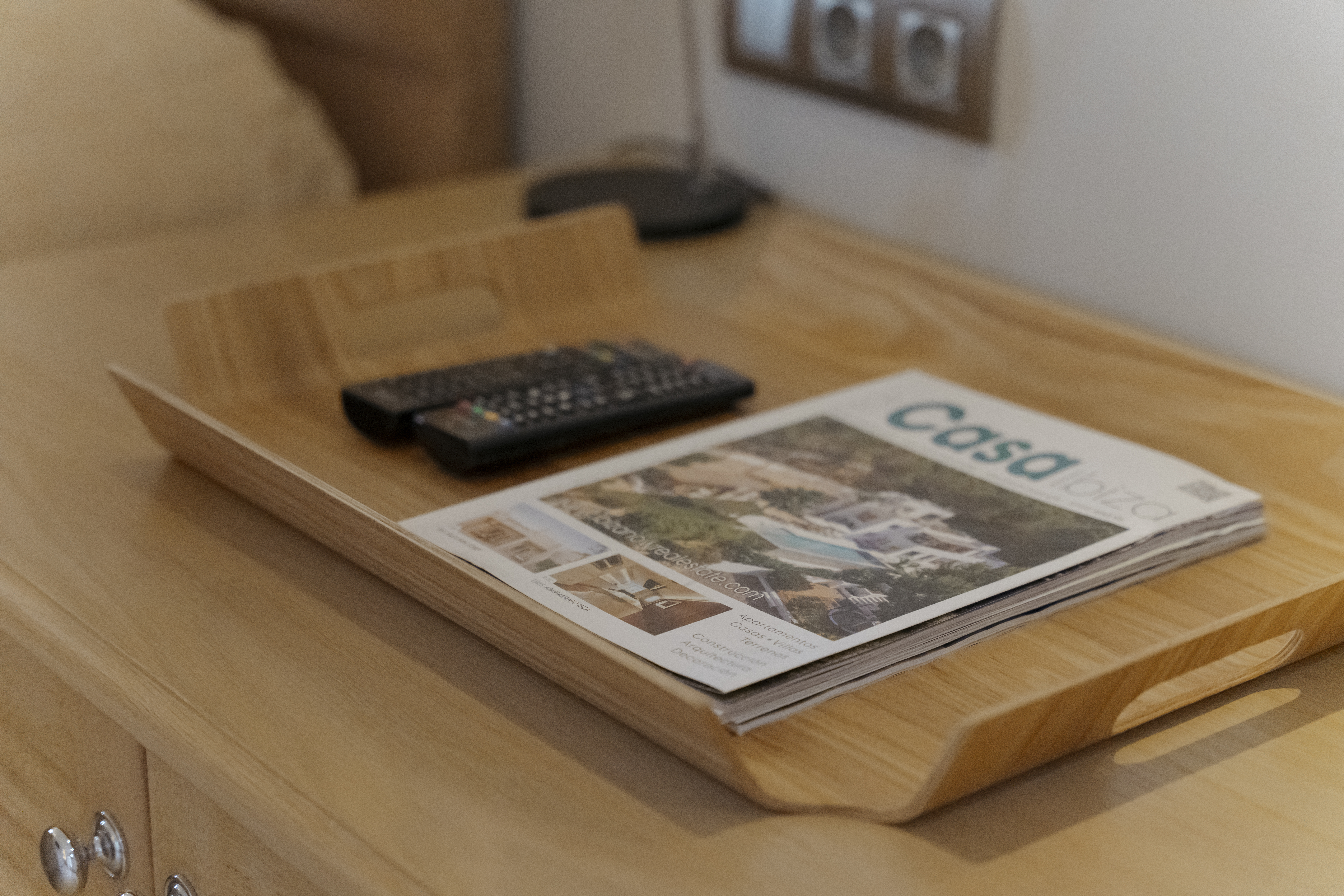 Welcome tray with remote controls and a local guide magazine on a wooden nightstand in a villa bedroom.