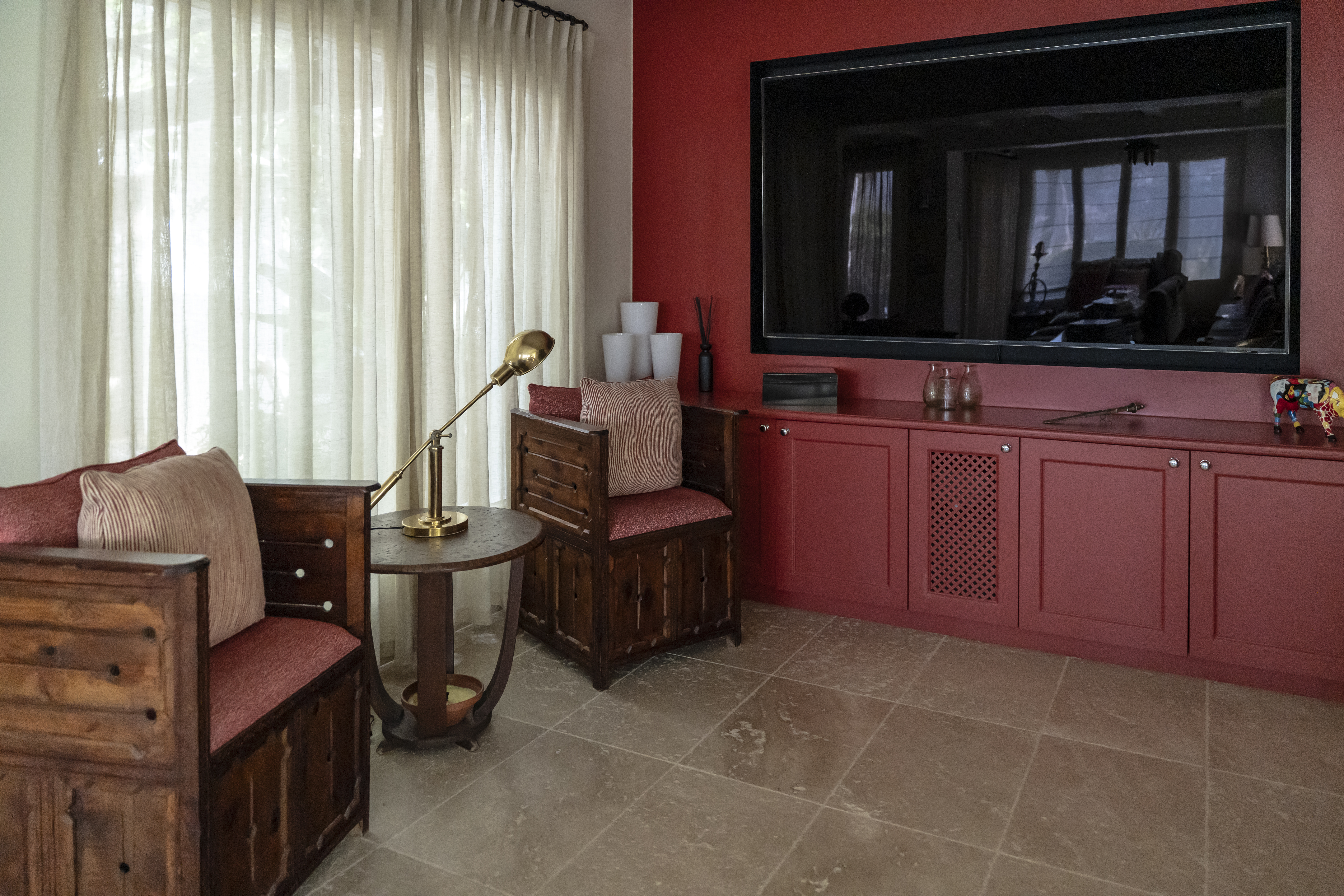 Cozy villa living room with custom red cabinetry, rustic wooden armchairs, and a large flat-screen TV.