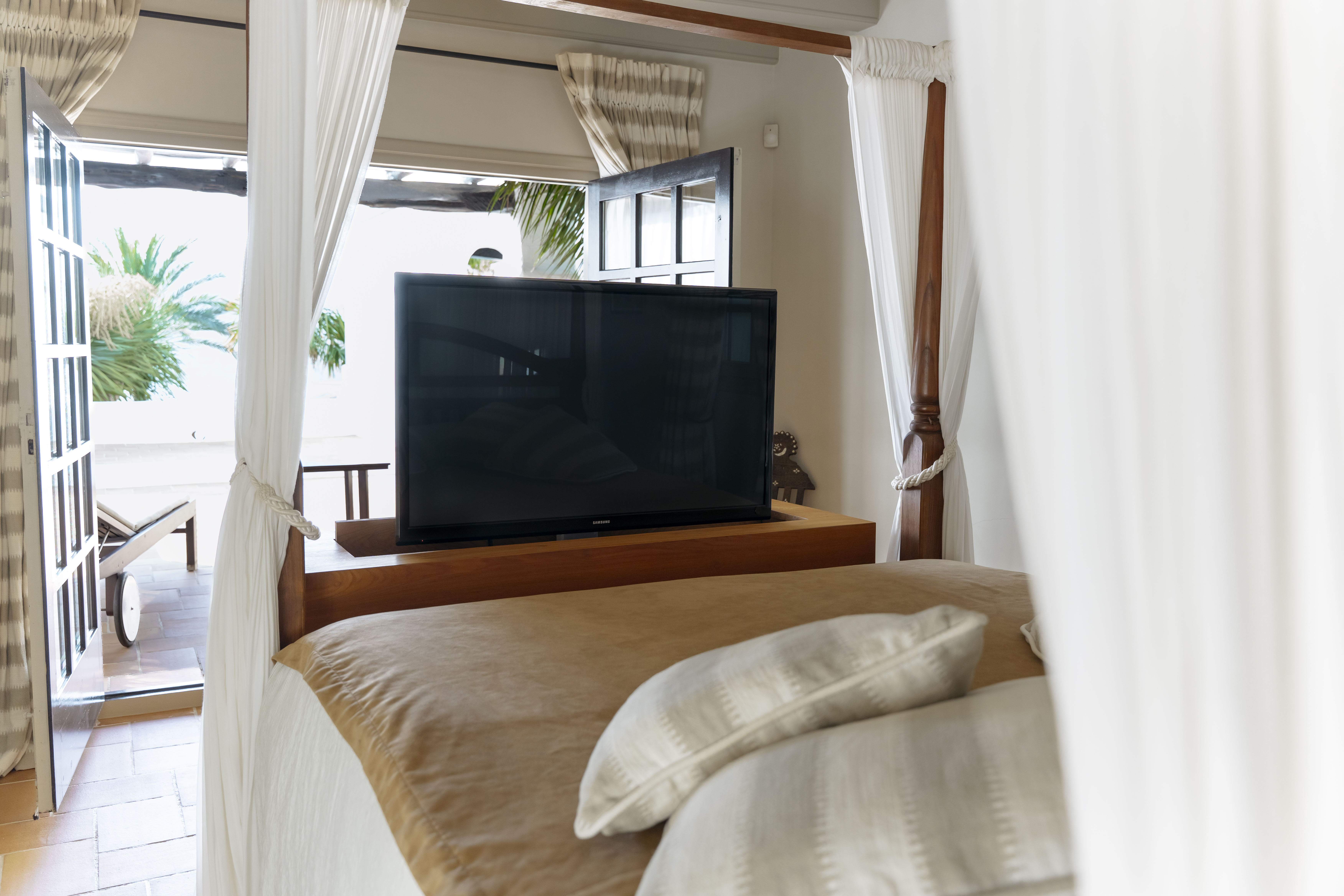 Luxury four-poster bed with an integrated pop-up TV screen and open doors to a private terrace.