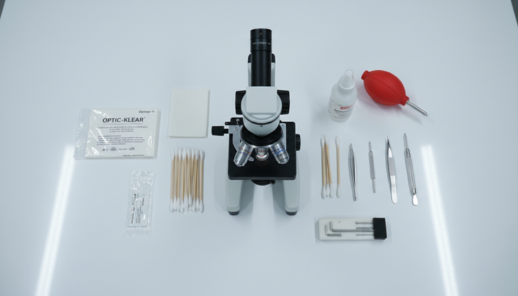 Overhead view of microscope tools and lens cleaning supplies beside a laboratory microscope.
