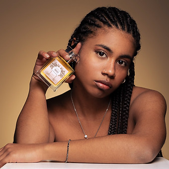 Giovane donna tiene profumo con etichetta, sfondo neutro. GB Photography.