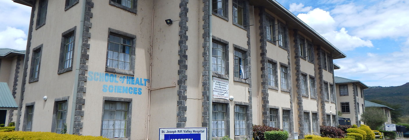 Tan stucco 3-storey buiding with grey bricks. Blue letters saying "School of Health Sciences" and sign saying "St. Joseph Rift Valley Hospital"