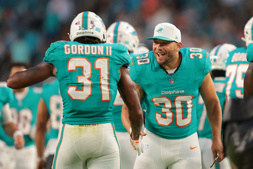 Two football players in teal jerseys, numbered 30 and 31, celebrate on the field. Both smile energetically in a stadium setting.