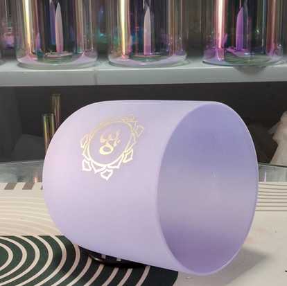 Paarse glazen beker met gouden logo, elegant design op een tafel.