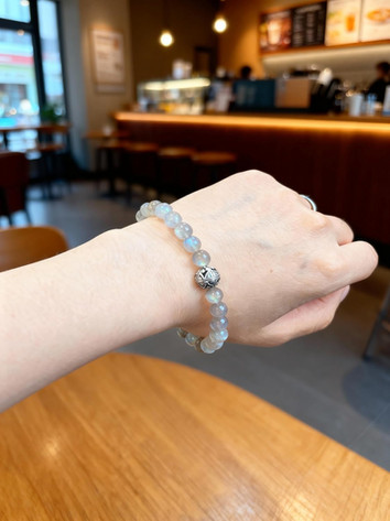 Hand met armband, close-up. Lichtgrijze kralen. Achtergrond met café interieur.