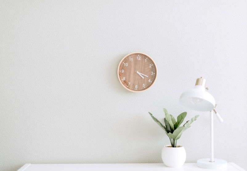 Clean business support work environment with a white desk, a pot plant, a lamp, and a clock.