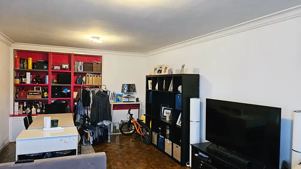 Salon avant rénovation avec grande bibliothèque rouge, meubles de rangement noirs et sol en parquet ancien.