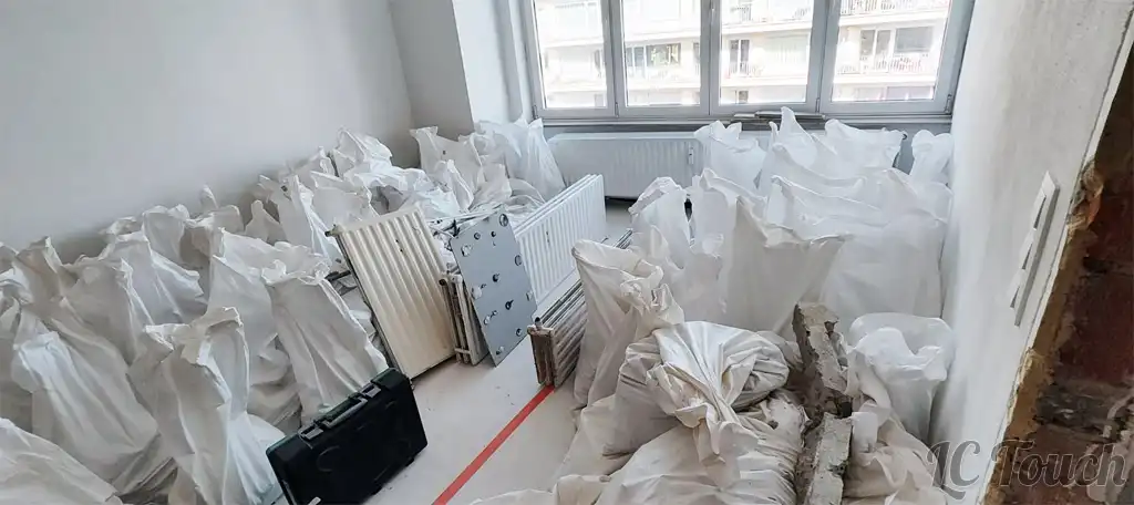 Accumulation de sacs de gravats et radiateurs démontés dans une pièce en rénovation avant l’évacuation des déchets du chantier.