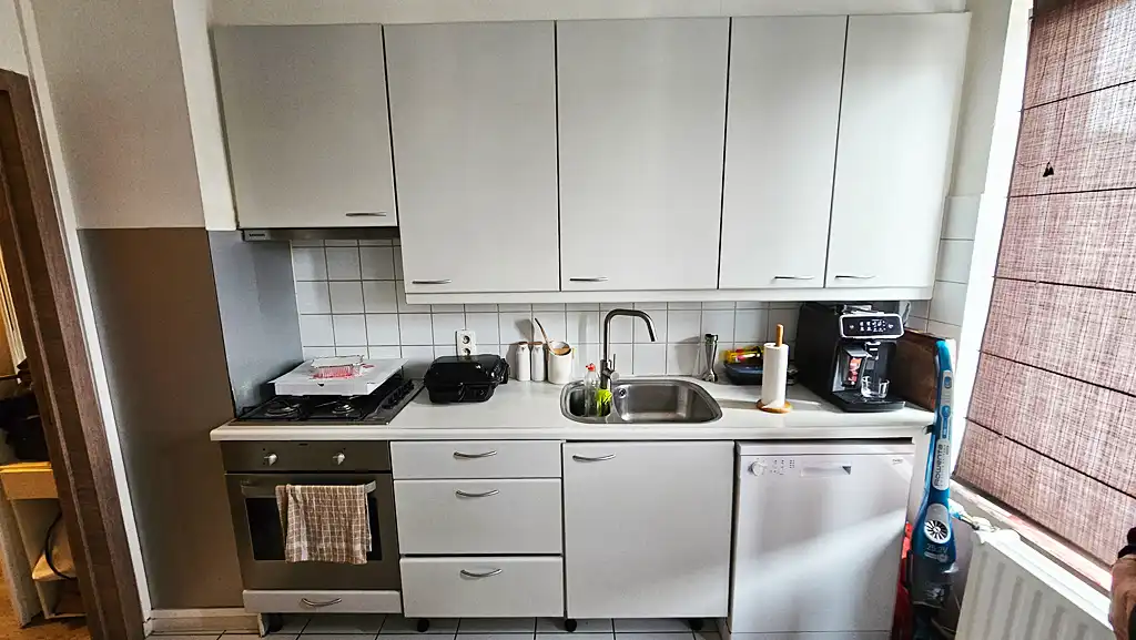 Cuisine existante avant rénovation avec meubles blancs, évier inox, cuisinière intégrée et crédence carrelée.