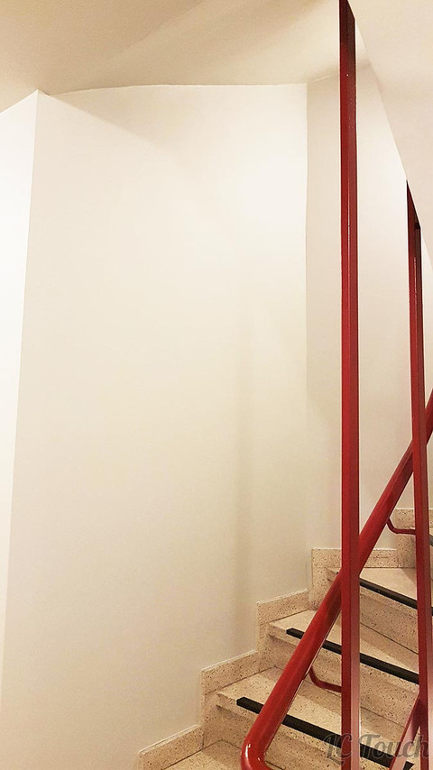 Cage d'escalier récemment rénovée avec des murs blancs et une rambarde rouge.