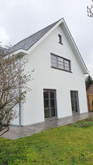 Maison moderne avec façade blanche, toiture en ardoise et jardin arboré.