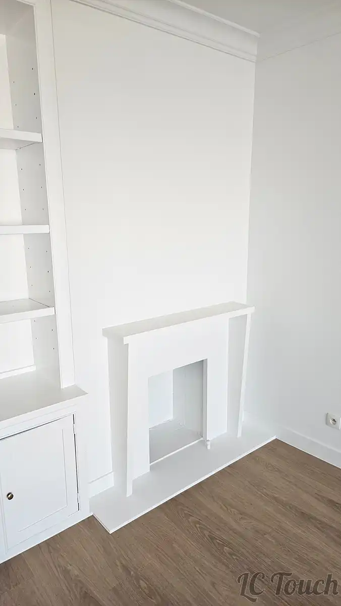 Cheminée décorative rénovée et peinte en blanc, intégrée à un salon modernisé avec sol en vinyle imitation bois