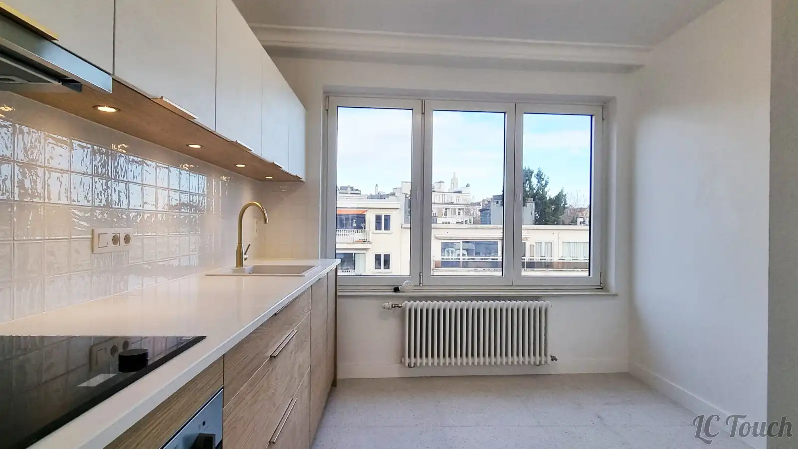 Cuisine rénovée à Bruxelles avec crédence carrelée blanche, plan de travail moderne et large fenêtre offrant une vue dégagée.