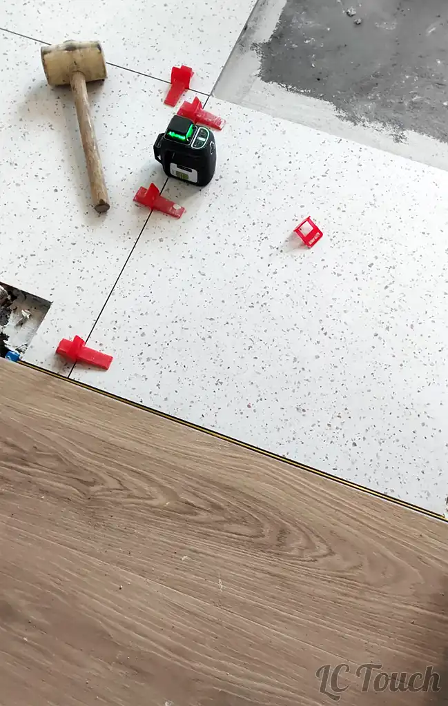 Ajustement du carrelage terrazzo avec cales de nivellement et transition prévue vers le revêtement vinyle imitation bois