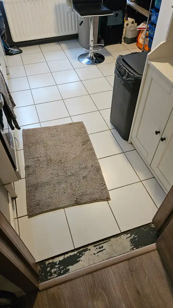 Sol de cuisine avant rénovation avec ancien carrelage blanc et seuil abîmé entre cuisine et pièce voisine.