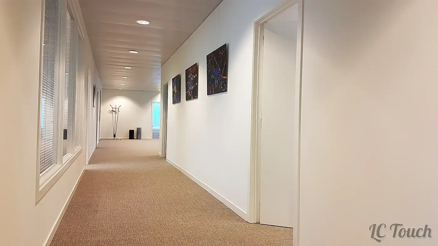Couloir d’entreprise rénové avec dalles de moquette amovibles, murs peints en blanc et éclairage encastré