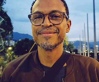Smiling radio personality wearing glasses, brown jacket