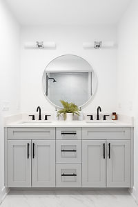 A renovated bathroom with a grey vanity cabinet, circular mirror with a view to a shower,