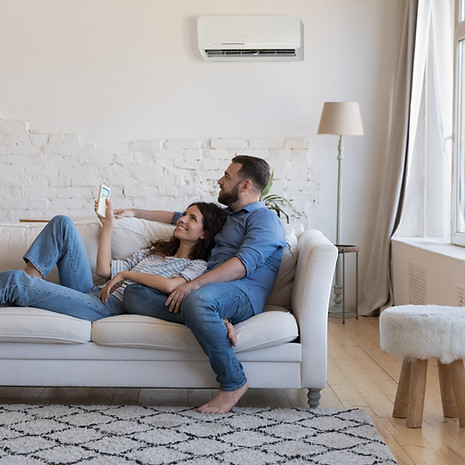 Happy millennial couple of homeowners enjoying cool conditioned air, resting on couch toge