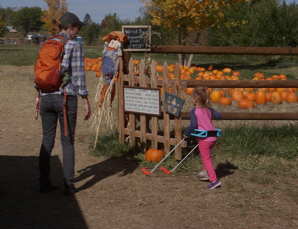 Woman and child wearing a Belt Cane at a pumpkin patch by a scarecrow sign reading Wrist Band beyond this point.